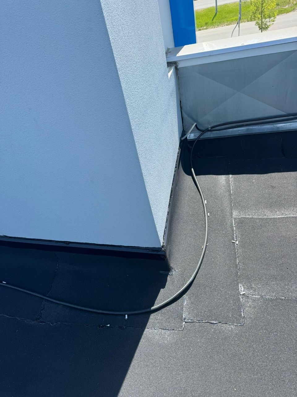 Aged flat roof membrane with visible seams at a stucco wall corner