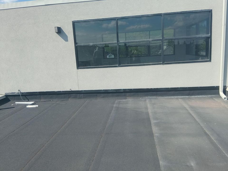 Flat roof membrane along the base of a stucco wall below a window