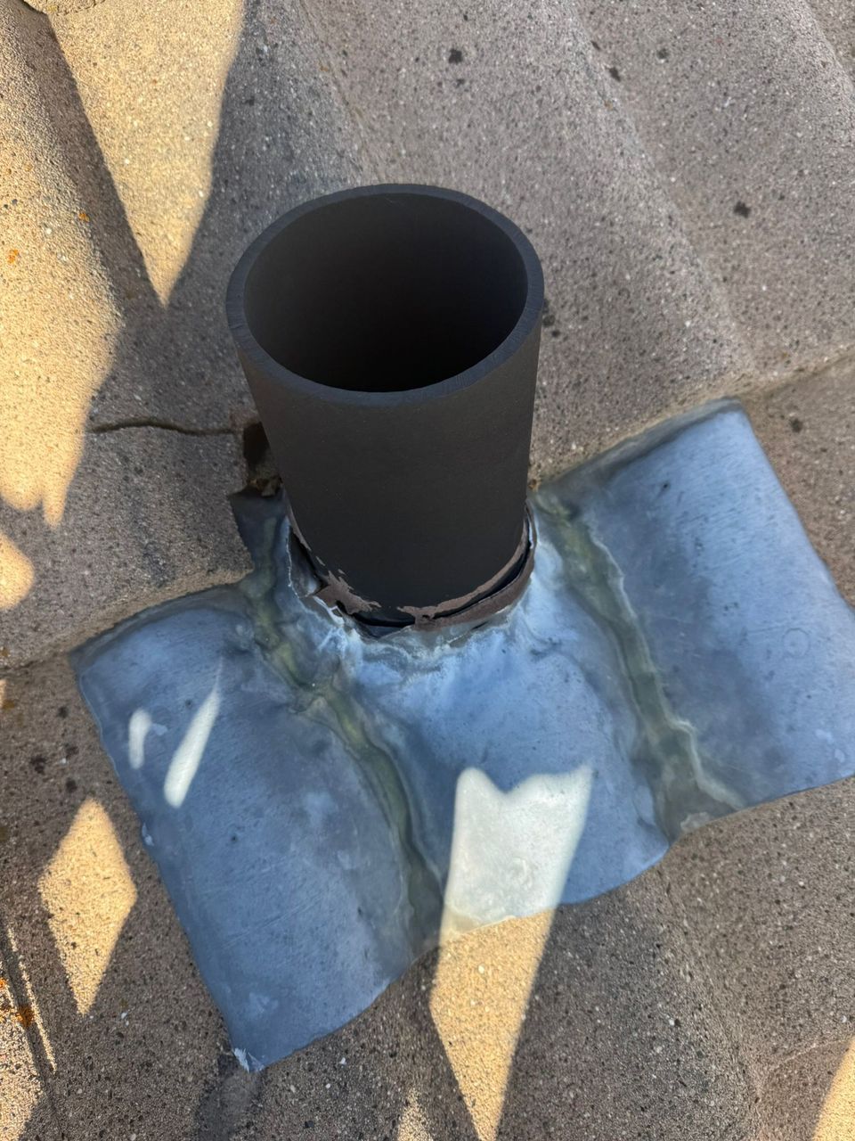Close-up of lead flashing and sealant around a vent pipe on a concrete tile roof