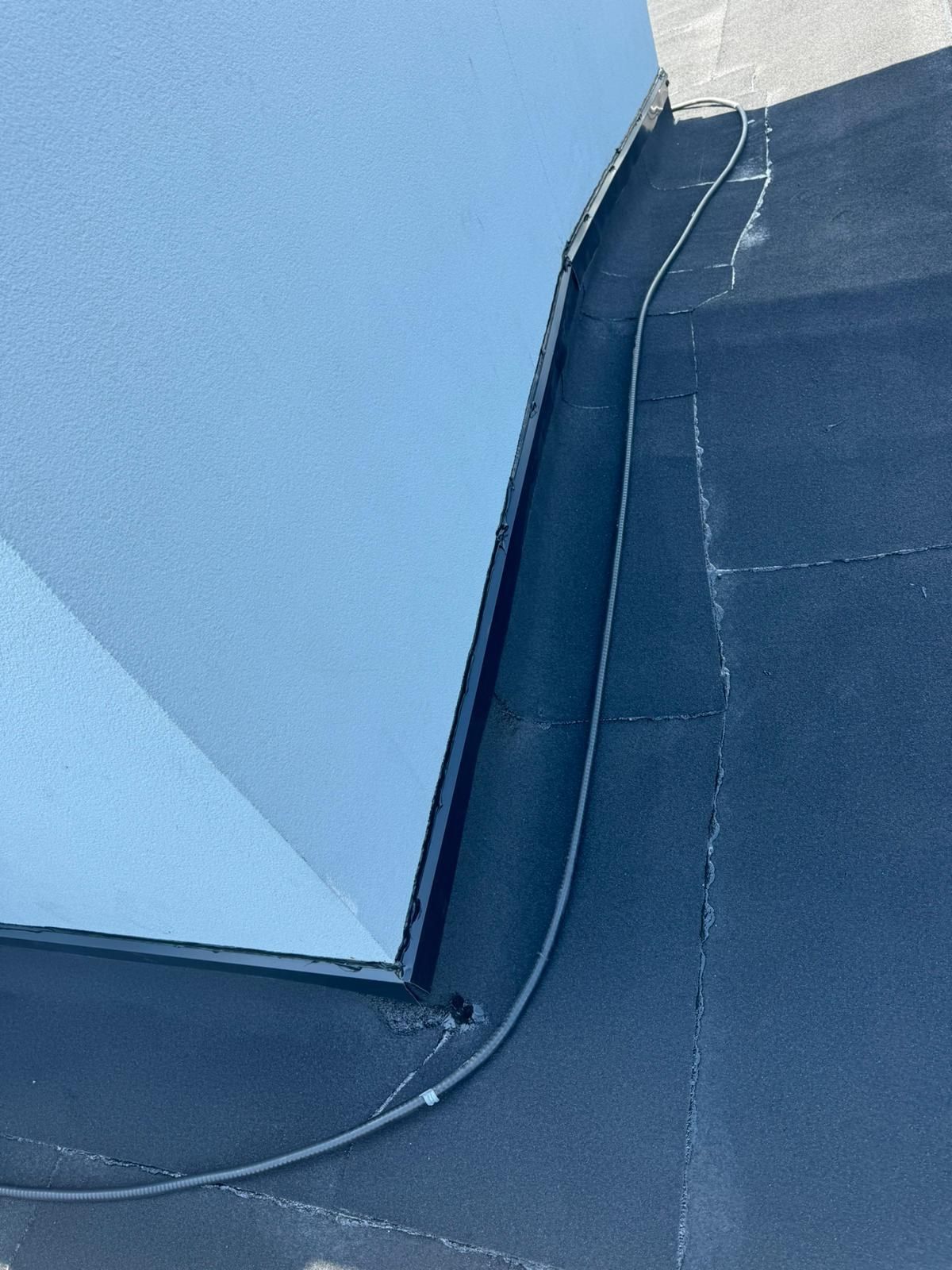 Open seams on an aged flat roof membrane running along a stucco wall in Calgary